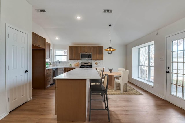 kitchen with hanging light fixtures, vaulted ceiling, light hardwood / wood-style floors, a kitchen island, and stainless steel appliances