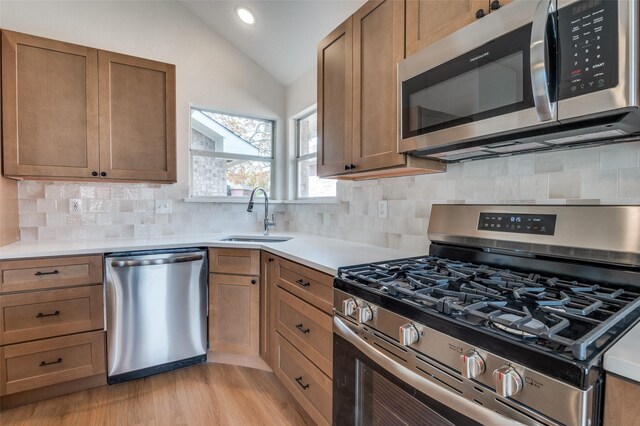 kitchen featuring stainless steel appliances, vaulted ceiling, tasteful backsplash, and sink