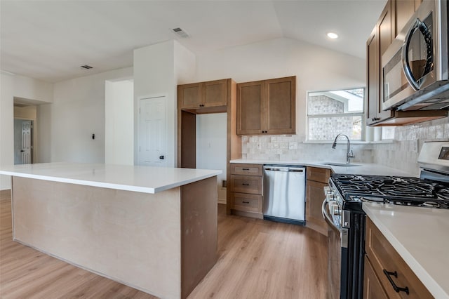 kitchen with tasteful backsplash, stainless steel appliances, vaulted ceiling, sink, and light hardwood / wood-style flooring