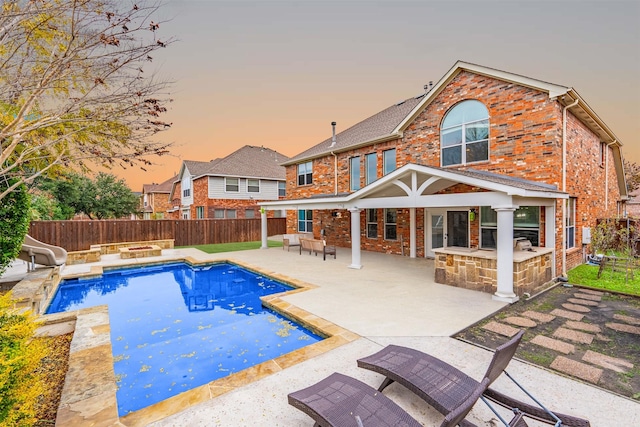 pool at dusk with a water slide, a patio, and exterior kitchen