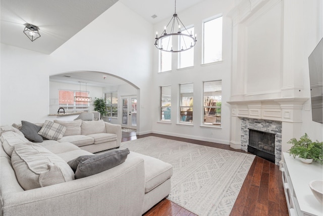 living room with dark hardwood / wood-style floors, a stone fireplace, a high ceiling, and an inviting chandelier