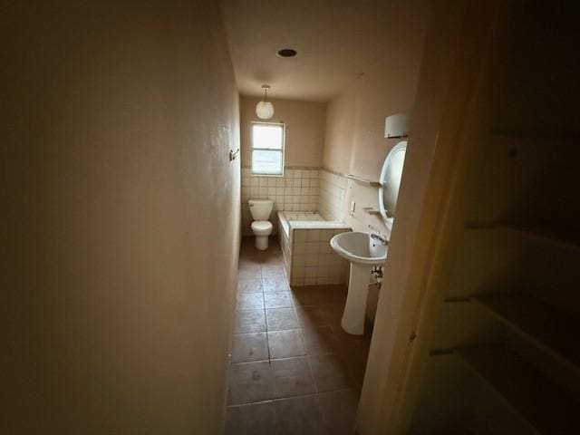 bathroom with a bathing tub, sink, tile patterned flooring, toilet, and tile walls