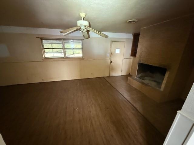 unfurnished living room featuring a fireplace, ceiling fan, and dark hardwood / wood-style flooring