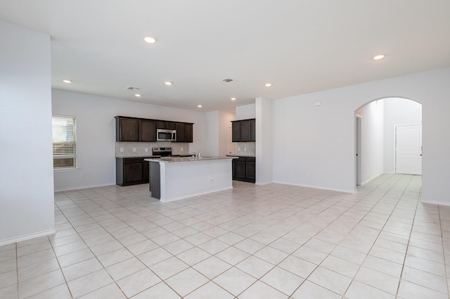 kitchen with dark brown cabinetry, stainless steel appliances, sink, light tile patterned floors, and a center island with sink