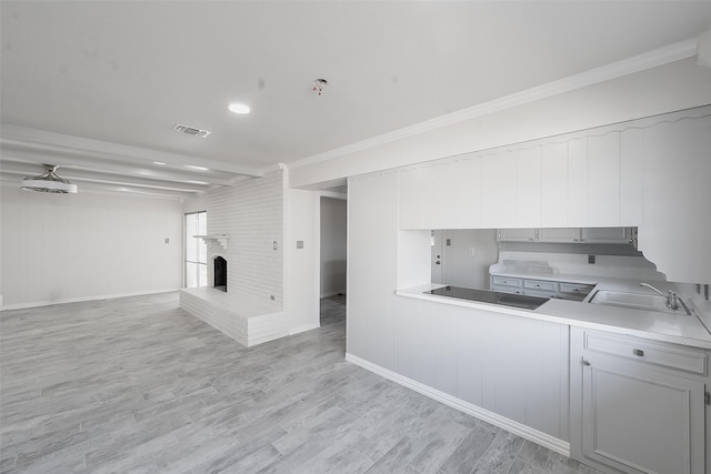 kitchen with sink, a brick fireplace, beamed ceiling, light hardwood / wood-style floors, and ornamental molding