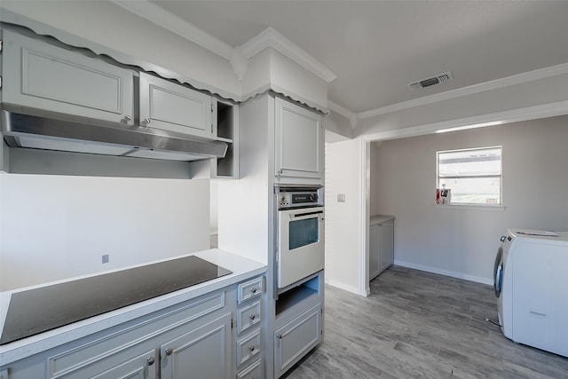 kitchen featuring stainless steel oven, independent washer and dryer, crown molding, gray cabinets, and light wood-type flooring