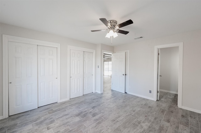 unfurnished bedroom featuring ceiling fan, light hardwood / wood-style flooring, and two closets