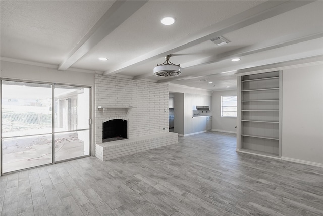 unfurnished living room with beamed ceiling, a brick fireplace, a textured ceiling, and light hardwood / wood-style flooring