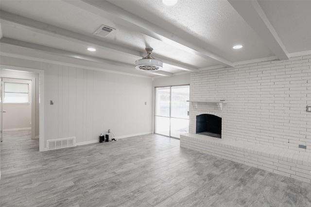 unfurnished living room with beam ceiling, light hardwood / wood-style flooring, a textured ceiling, and a brick fireplace