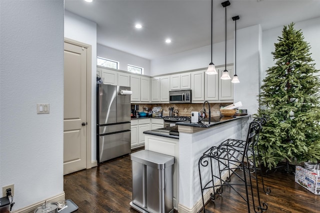 kitchen featuring kitchen peninsula, appliances with stainless steel finishes, tasteful backsplash, decorative light fixtures, and white cabinets