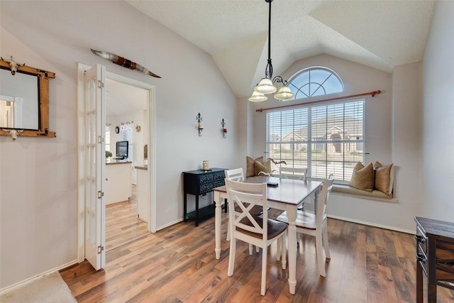 dining room featuring a notable chandelier, wood-type flooring, lofted ceiling, and a textured ceiling