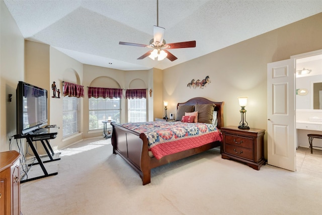 bedroom featuring lofted ceiling, ensuite bath, ceiling fan, a textured ceiling, and light colored carpet