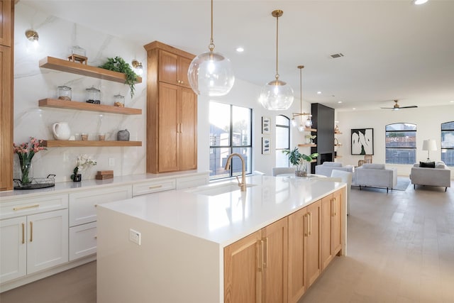 kitchen with white cabinetry, sink, hanging light fixtures, a center island with sink, and light hardwood / wood-style flooring