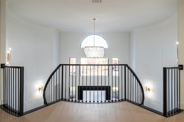 corridor with an inviting chandelier, wood-type flooring, ornamental molding, radiator heating unit, and a towering ceiling