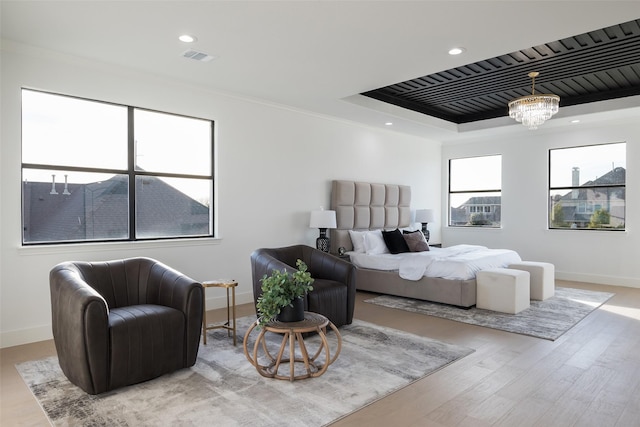 bedroom featuring ornamental molding, light hardwood / wood-style floors, a raised ceiling, and a chandelier