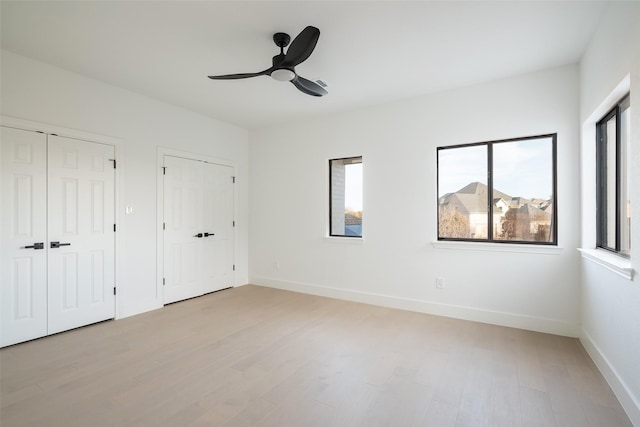 unfurnished bedroom with multiple closets, ceiling fan, light hardwood / wood-style floors, and multiple windows