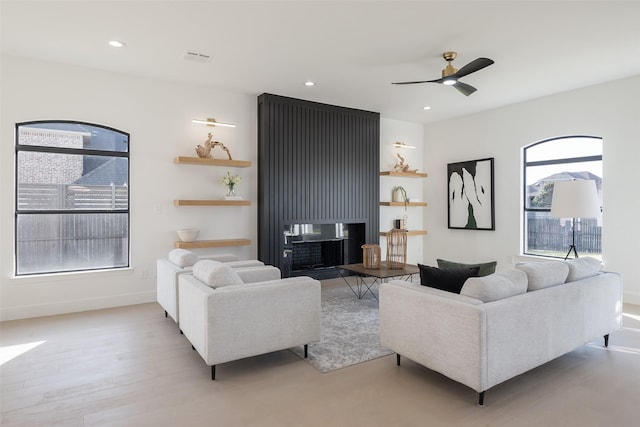 living room featuring a multi sided fireplace, light wood-type flooring, and ceiling fan