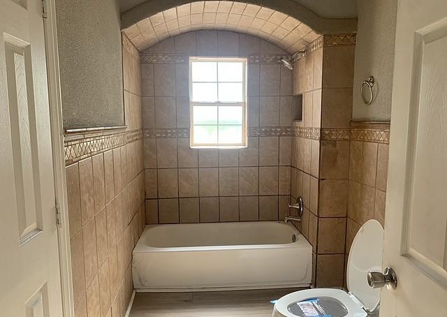 bathroom featuring toilet, wood-type flooring, and tiled shower / bath