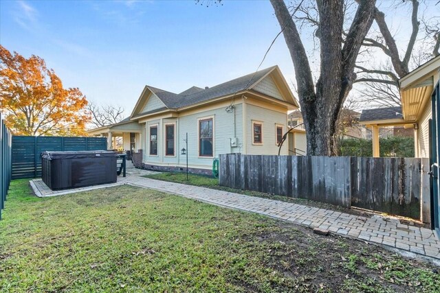 rear view of property with a hot tub and a lawn