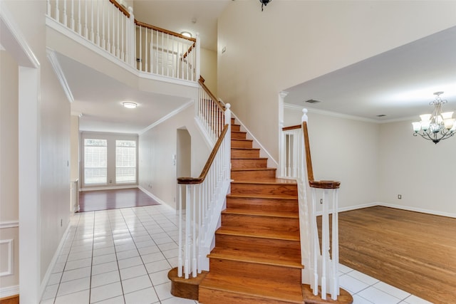 staircase featuring wood-type flooring, a towering ceiling, crown molding, and a notable chandelier