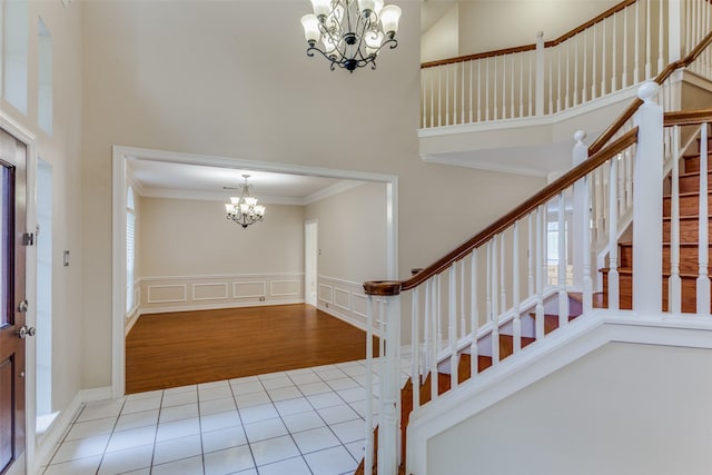 entrance foyer featuring ornamental molding, a towering ceiling, light wood-type flooring, and a notable chandelier