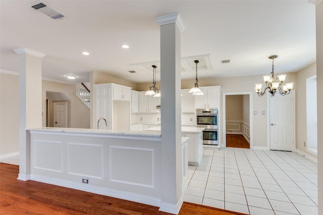 kitchen with white cabinets, a notable chandelier, stainless steel double oven, and light hardwood / wood-style flooring