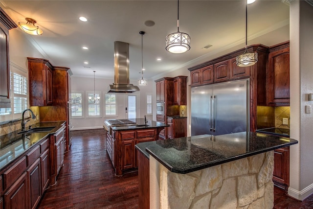 kitchen with built in appliances, a center island, hanging light fixtures, dark stone countertops, and island exhaust hood