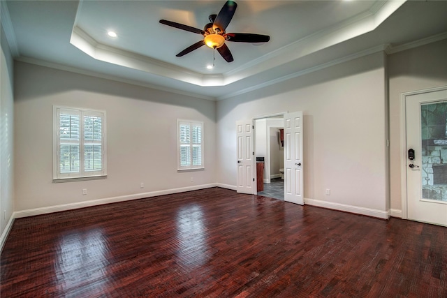 empty room with dark wood-type flooring, ceiling fan, a tray ceiling, and crown molding