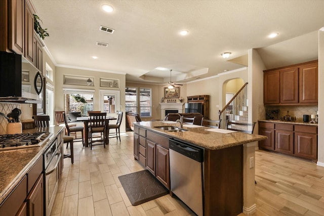 kitchen featuring backsplash, a kitchen island with sink, ceiling fan, ornamental molding, and stainless steel appliances