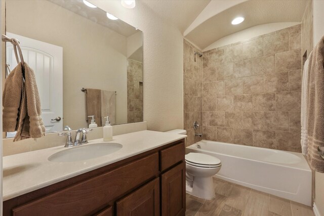 full bathroom with hardwood / wood-style floors, vanity, tiled shower / bath combo, and toilet