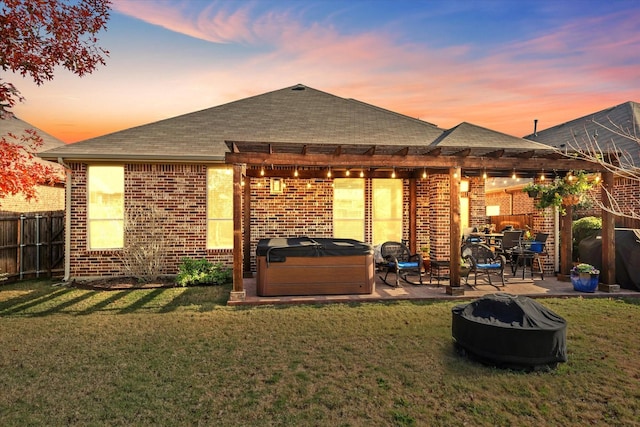 back house at dusk with a lawn, a patio area, and a hot tub