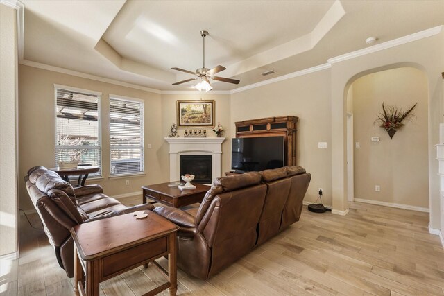 living room featuring a raised ceiling, ceiling fan, light hardwood / wood-style floors, and ornamental molding