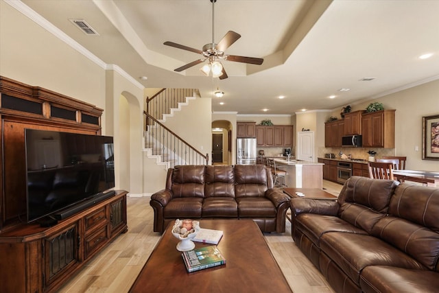 living room with ceiling fan, light wood-type flooring, ornamental molding, and a tray ceiling