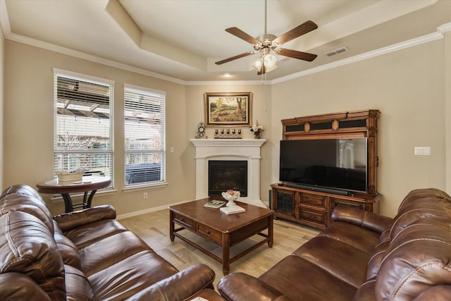 living room with ceiling fan, light wood-type flooring, ornamental molding, and a tray ceiling