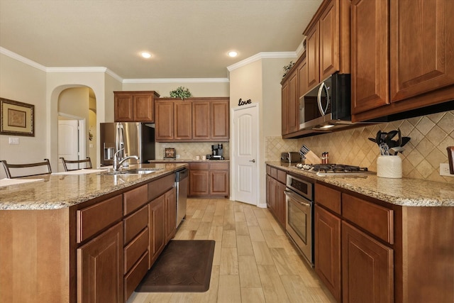 kitchen with light stone countertops, appliances with stainless steel finishes, crown molding, sink, and an island with sink