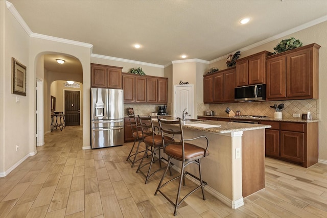 kitchen with a center island with sink, light hardwood / wood-style flooring, appliances with stainless steel finishes, light stone counters, and a breakfast bar area