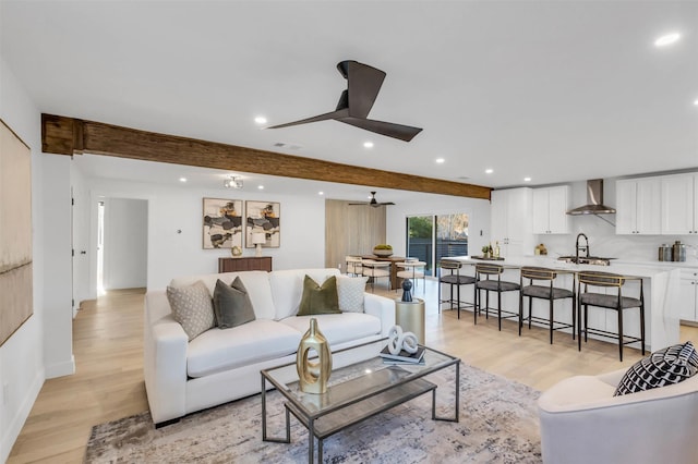 living room featuring beam ceiling, light hardwood / wood-style flooring, ceiling fan, and sink