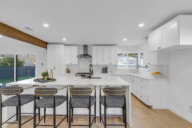 kitchen with light hardwood / wood-style flooring, white cabinetry, a wealth of natural light, and wall chimney exhaust hood