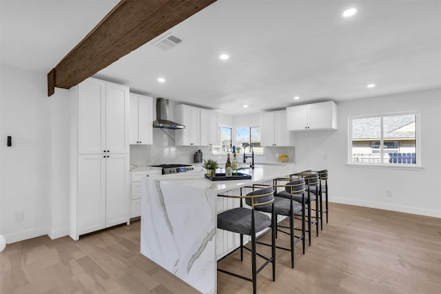 kitchen featuring beamed ceiling, wall chimney exhaust hood, a center island, and white cabinets