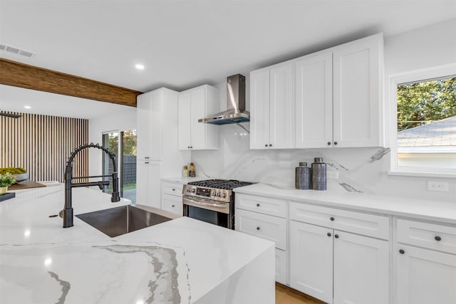 kitchen with a wealth of natural light, stainless steel range, white cabinets, and wall chimney range hood