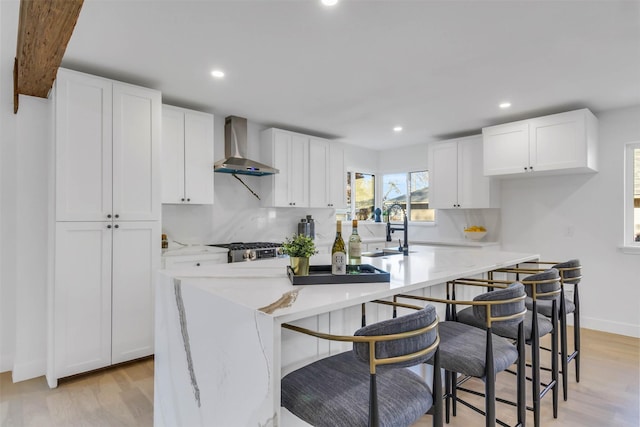 kitchen featuring light wood-type flooring, wall chimney exhaust hood, sink, a center island, and white cabinetry