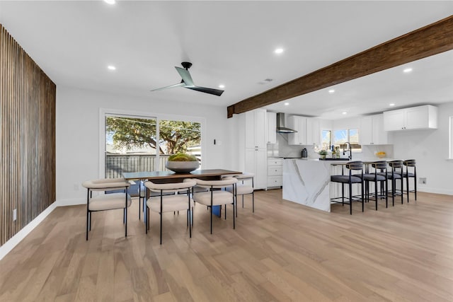 dining area with beam ceiling, light hardwood / wood-style flooring, ceiling fan, and wood walls