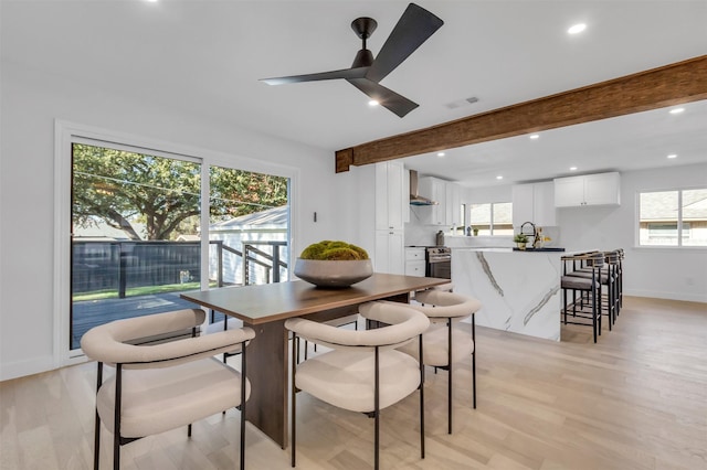 dining area featuring beamed ceiling, light wood-type flooring, ceiling fan, and sink