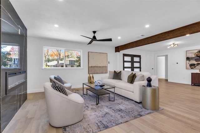 living room featuring beamed ceiling, ceiling fan, and light wood-type flooring