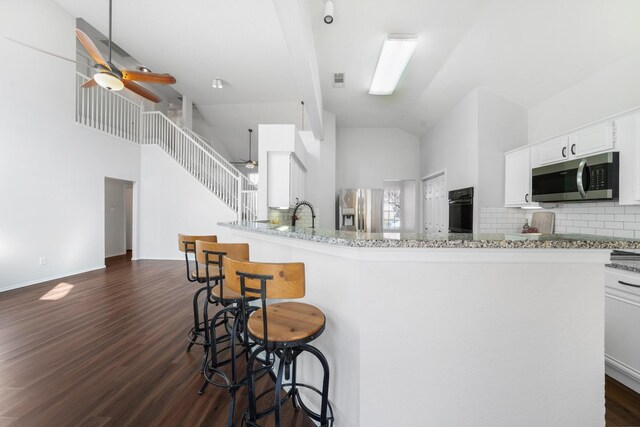 kitchen featuring a breakfast bar, high vaulted ceiling, white cabinets, dark hardwood / wood-style floors, and stainless steel appliances