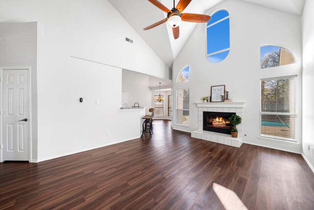 unfurnished living room featuring ceiling fan, dark hardwood / wood-style flooring, high vaulted ceiling, and a tiled fireplace