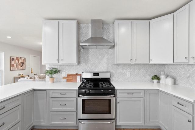 kitchen featuring gray cabinetry, gas stove, decorative backsplash, and wall chimney range hood