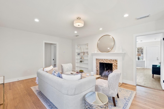 living room with built in features, light hardwood / wood-style flooring, and a tiled fireplace