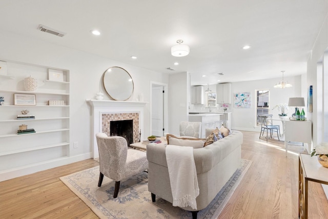 living room with a tiled fireplace, a chandelier, built in shelves, and light hardwood / wood-style floors