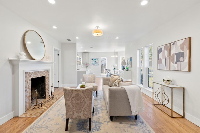 living room with a chandelier, light hardwood / wood-style flooring, and a tiled fireplace